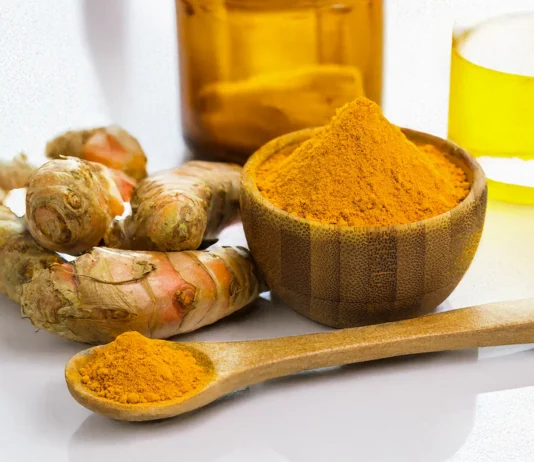 A wooden bowl and spoon containing pure turmeric curcumin powder